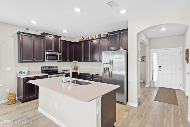 kitchen featuring stainless steel appliances, dark brown cabinets, sink, and a center island with sink