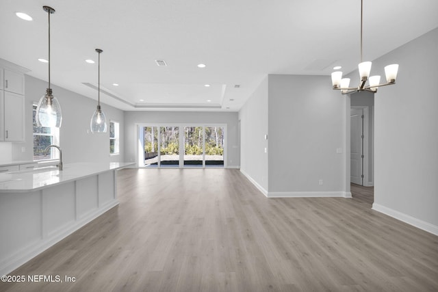 unfurnished living room with an inviting chandelier, a raised ceiling, sink, and light wood-type flooring