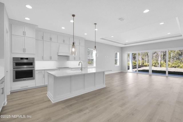 kitchen featuring hanging light fixtures, double oven, custom exhaust hood, and a center island with sink