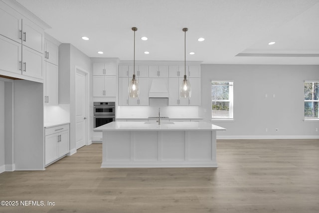 kitchen featuring white cabinets, hanging light fixtures, and a center island with sink