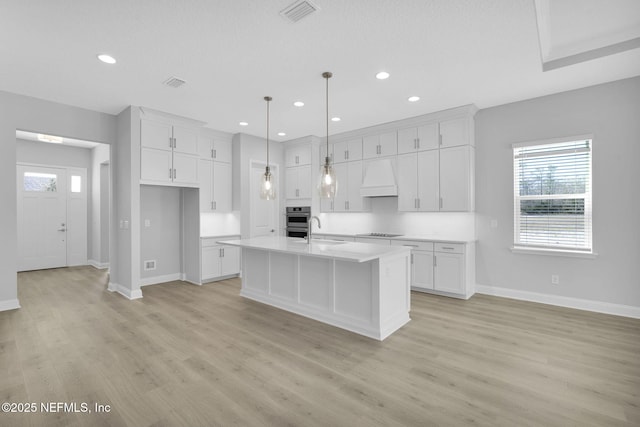 kitchen featuring premium range hood, decorative light fixtures, white cabinetry, a kitchen island with sink, and black electric stovetop