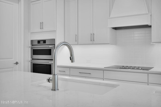 kitchen featuring white cabinetry, tasteful backsplash, light stone countertops, and custom exhaust hood