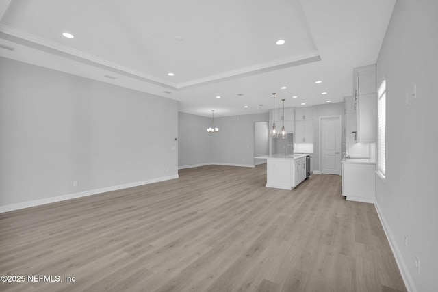 unfurnished living room with sink, crown molding, a raised ceiling, a notable chandelier, and light hardwood / wood-style floors