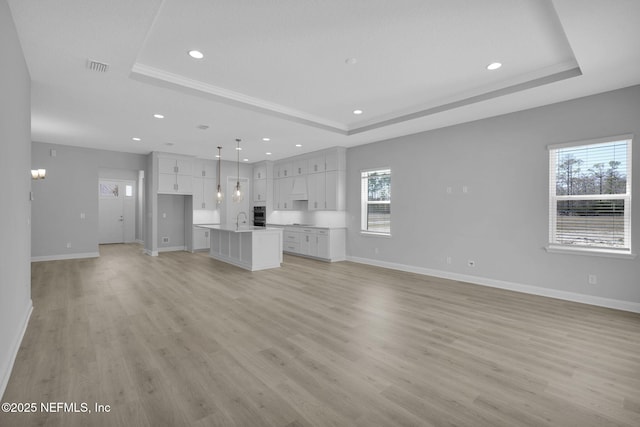 unfurnished living room with sink, light hardwood / wood-style flooring, and a raised ceiling