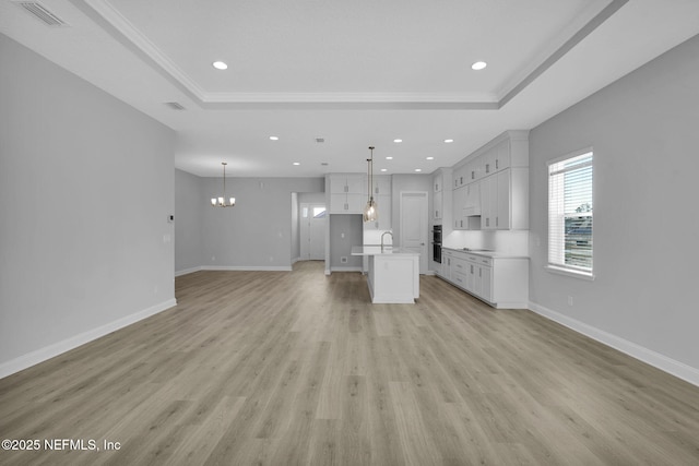 unfurnished living room with sink, light hardwood / wood-style flooring, a notable chandelier, a tray ceiling, and ornamental molding