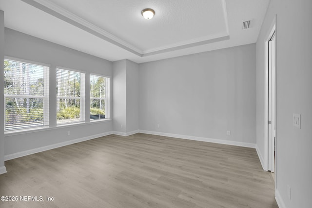 empty room featuring a tray ceiling, light hardwood / wood-style flooring, and a textured ceiling