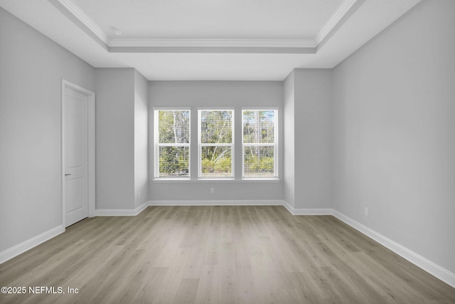 empty room with ornamental molding, a tray ceiling, and light hardwood / wood-style flooring