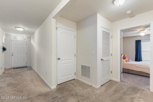 hallway with light colored carpet and a textured ceiling