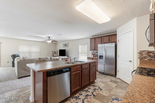 kitchen with appliances with stainless steel finishes, an island with sink, sink, ceiling fan, and a textured ceiling