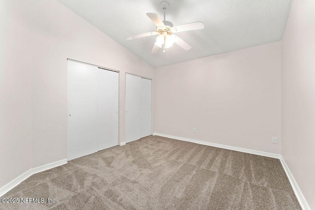 unfurnished bedroom with vaulted ceiling, a textured ceiling, carpet flooring, two closets, and ceiling fan