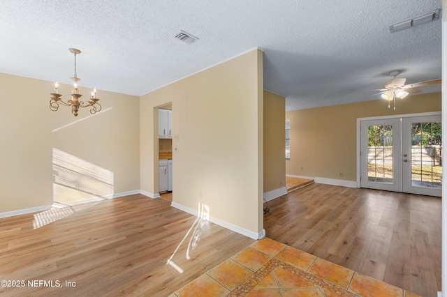 unfurnished room featuring french doors, ceiling fan with notable chandelier, a textured ceiling, and light wood-type flooring