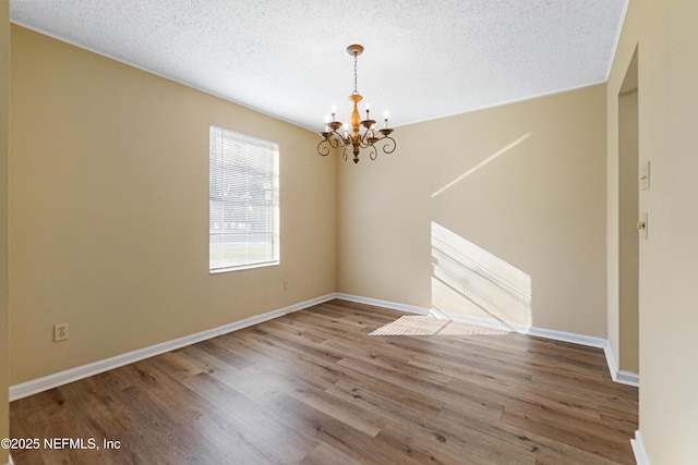 spare room featuring a chandelier, hardwood / wood-style floors, and a textured ceiling