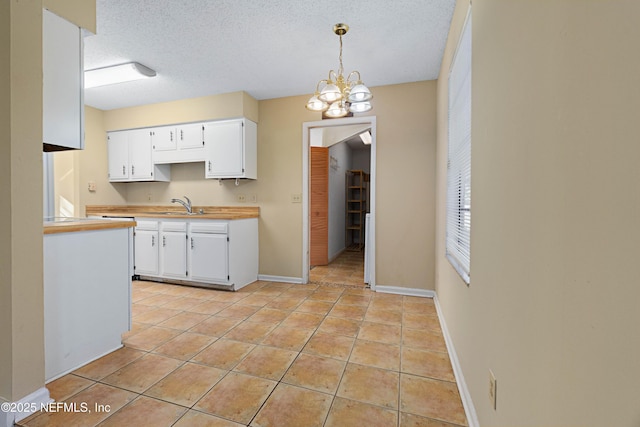 kitchen with sink, a textured ceiling, light tile patterned floors, pendant lighting, and white cabinets