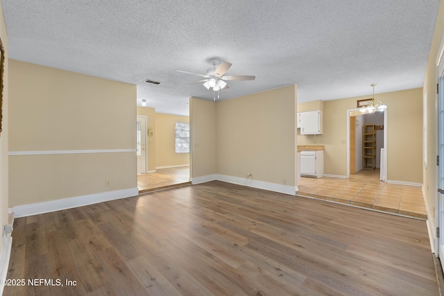 unfurnished living room featuring ceiling fan with notable chandelier, a textured ceiling, and light hardwood / wood-style flooring