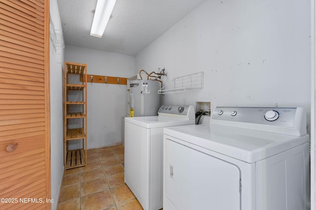 laundry room with washer and dryer, light tile patterned floors, water heater, and a textured ceiling