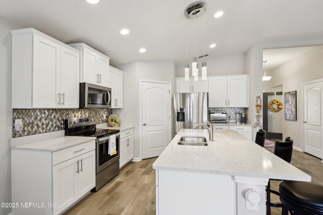 kitchen with an island with sink, appliances with stainless steel finishes, sink, and pendant lighting