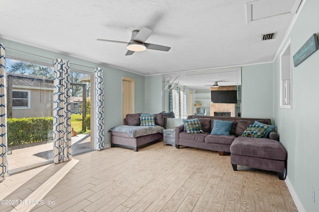 living area featuring ornamental molding, light wood-type flooring, a brick fireplace, and ceiling fan