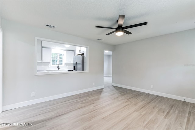 empty room featuring ceiling fan, sink, a textured ceiling, and light hardwood / wood-style flooring