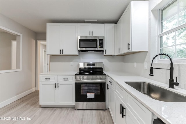 kitchen featuring sink, light stone counters, light wood-type flooring, stainless steel appliances, and white cabinets