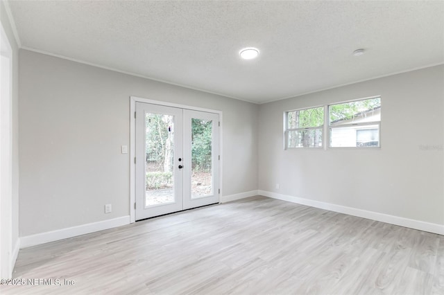 empty room with crown molding, french doors, a textured ceiling, and light wood-type flooring