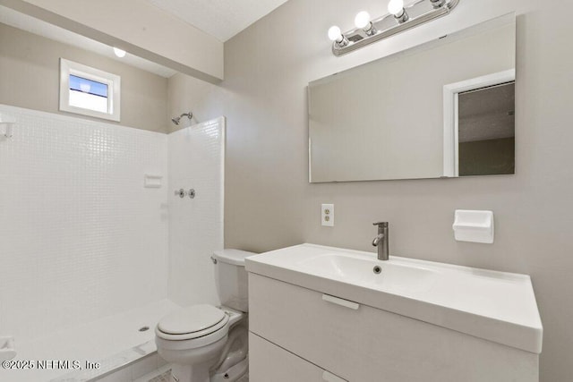 bathroom with vanity, a tile shower, and toilet