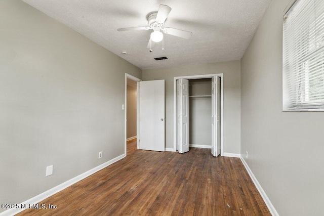 unfurnished bedroom with a textured ceiling, dark wood-type flooring, a closet, and ceiling fan