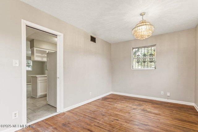 spare room featuring an inviting chandelier and light hardwood / wood-style flooring