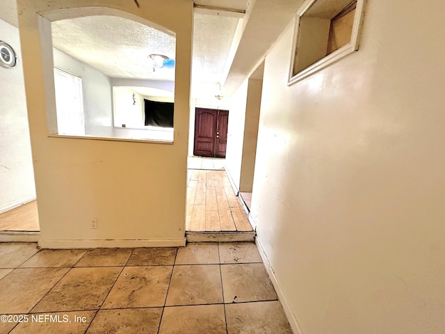 hall with a textured ceiling and light tile patterned floors