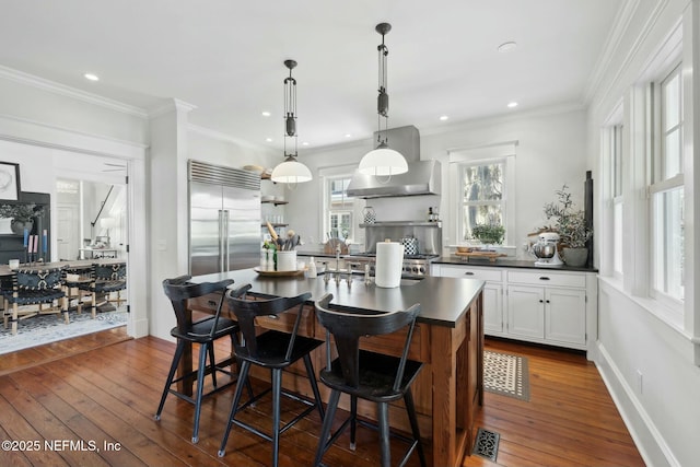 kitchen with dark hardwood / wood-style floors, stainless steel built in fridge, hanging light fixtures, and white cabinets