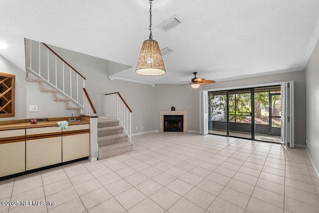 unfurnished living room featuring a textured ceiling, light tile patterned flooring, a tile fireplace, visible vents, and stairs