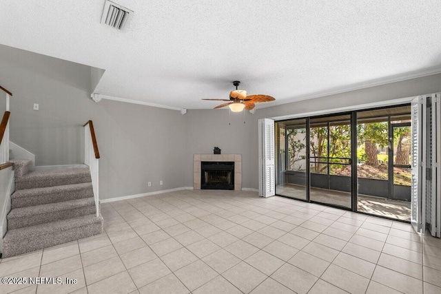 unfurnished living room featuring light tile patterned floors, visible vents, a ceiling fan, a tile fireplace, and stairway