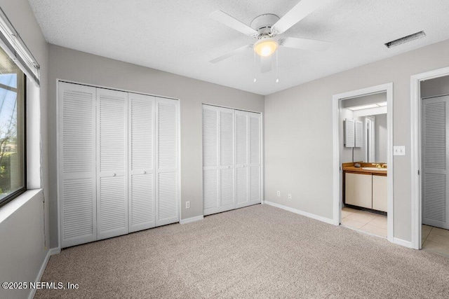 unfurnished bedroom featuring carpet floors, multiple windows, visible vents, and two closets