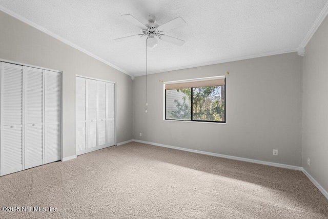 unfurnished bedroom featuring vaulted ceiling, carpet floors, ornamental molding, and two closets