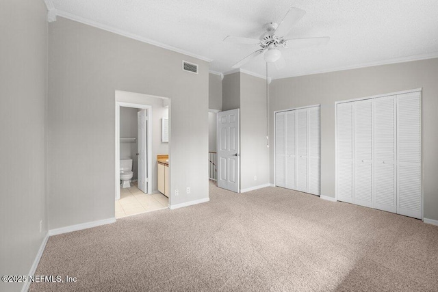 unfurnished bedroom with light carpet, visible vents, baseboards, ornamental molding, and two closets