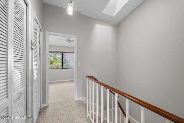 corridor featuring vaulted ceiling with skylight, baseboards, carpet flooring, and an upstairs landing