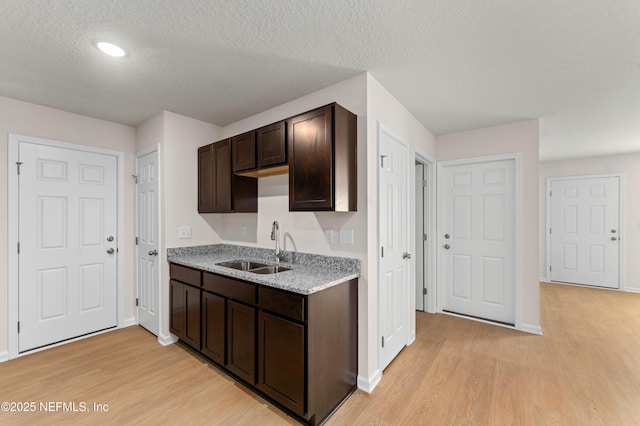 kitchen featuring a textured ceiling, sink, dark brown cabinets, and light wood-type flooring