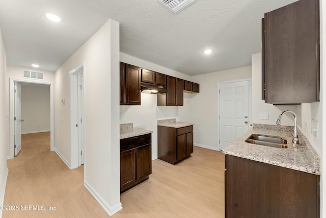 kitchen featuring dark brown cabinetry, sink, light hardwood / wood-style flooring, a textured ceiling, and light stone countertops