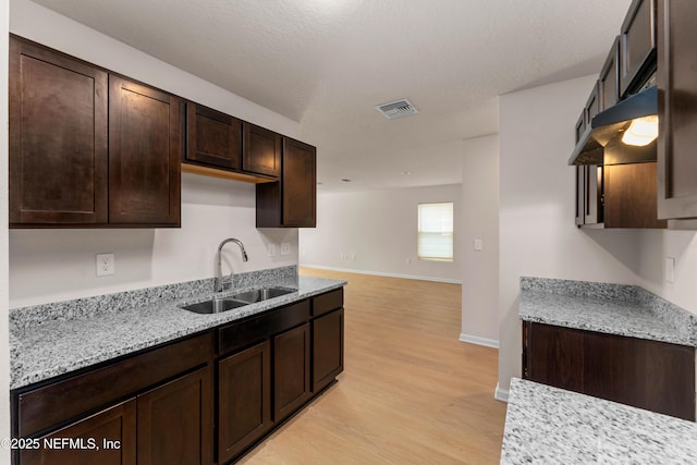 kitchen with dark brown cabinetry, sink, light hardwood / wood-style flooring, a textured ceiling, and light stone countertops