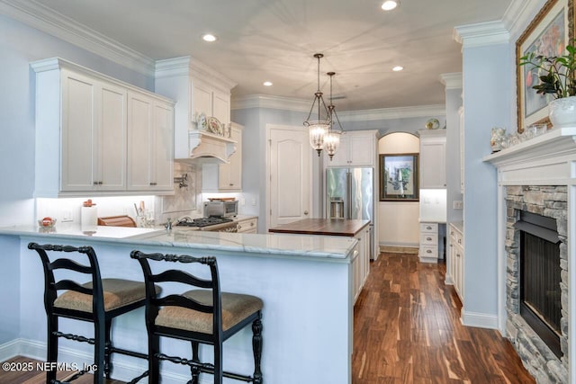 kitchen featuring a stone fireplace, pendant lighting, white cabinets, dark hardwood / wood-style flooring, and crown molding