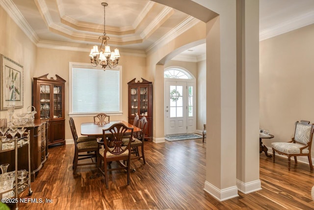 dining room with dark wood-type flooring, crown molding, a raised ceiling, and a notable chandelier