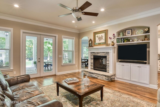 living room featuring a stone fireplace, a wealth of natural light, light wood-type flooring, and french doors