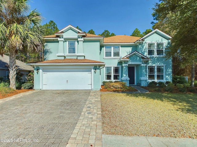 view of front of property featuring a front yard, decorative driveway, an attached garage, and stucco siding