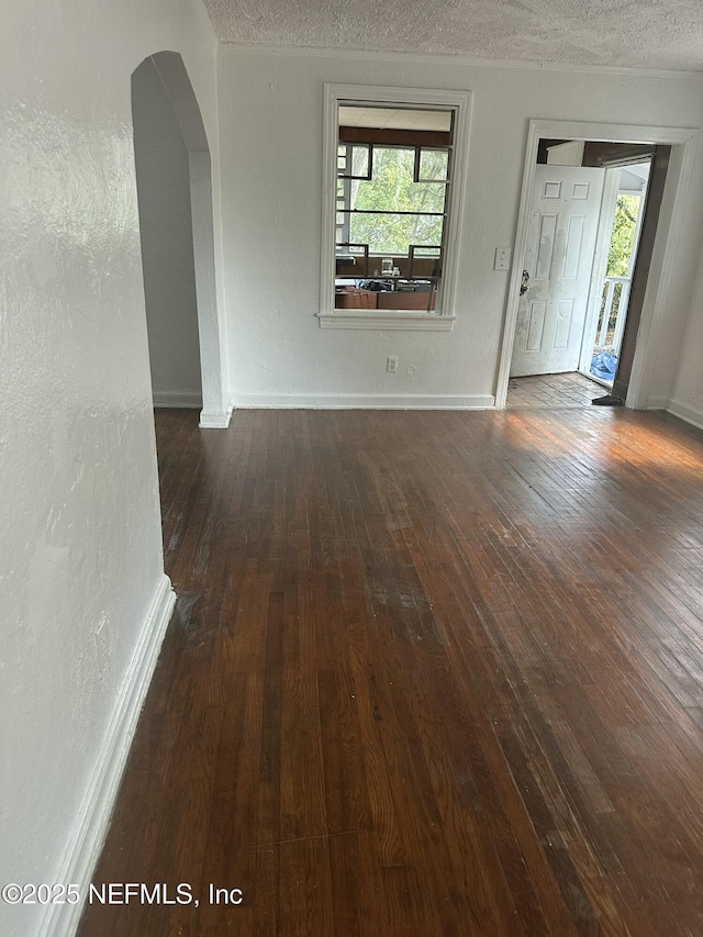 interior space with baseboards, a textured wall, a textured ceiling, arched walkways, and wood-type flooring