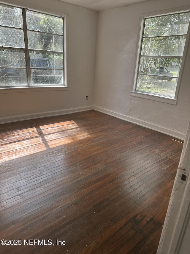 spare room featuring baseboards, dark wood finished floors, and plenty of natural light