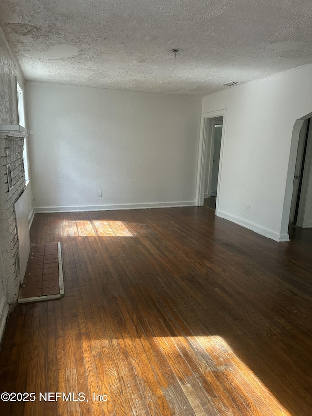 empty room featuring baseboards, arched walkways, a textured ceiling, a fireplace, and wood-type flooring