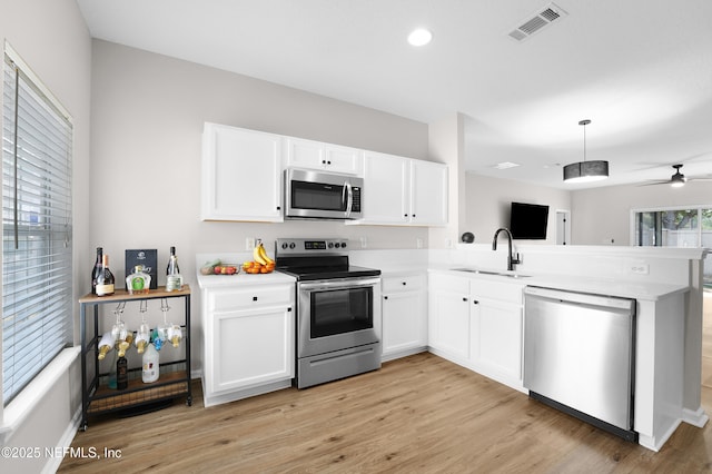 kitchen featuring appliances with stainless steel finishes, white cabinetry, sink, kitchen peninsula, and light wood-type flooring