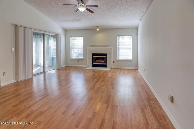 unfurnished living room featuring lofted ceiling, light hardwood / wood-style flooring, a tile fireplace, ceiling fan, and a textured ceiling