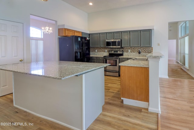 kitchen featuring appliances with stainless steel finishes, sink, backsplash, light stone counters, and light hardwood / wood-style floors