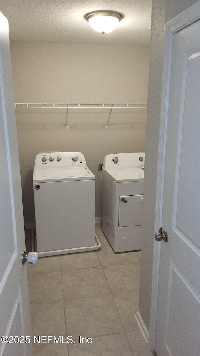 clothes washing area with washing machine and dryer, light tile patterned floors, and a textured ceiling