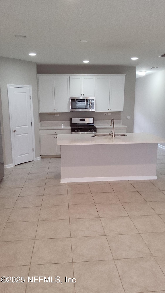 kitchen with appliances with stainless steel finishes, white cabinetry, an island with sink, sink, and light tile patterned floors